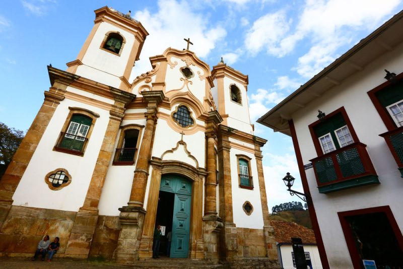 Vista frontal da Igreja de São Francisco de Assis em Ouro Preto, com arquitetura barroca, torres gêmeas e céu azul ao fundo